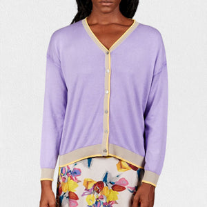 A woman wears the IN BED WITH YOU - BATWING SLEEVE CARDIGAN by IN BED WITH YOU/CLAUDIOLAI SRL, an orange V-neck with red and white trim, buttoned down the front, styled with multicolored patterned pants against a plain white background.