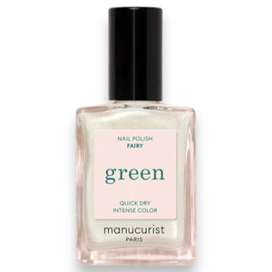 A person with light green painted nails holds a bottle of MANUCURIST INC’s GREEN™ Nail Polish in Fairy, wearing a purple knit top adorned with rhinestone embellishments.