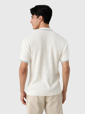 A smiling gray-haired man in sunglasses and khaki pants wears the CRIQUET Bungalow Sweater Polo in White, featuring a blue-trimmed collar and pocket, standing against a plain background.