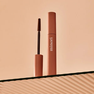 Three close-up shots of a blue eye: lashes with no mascara (before), lashes enhanced with MINORI - MOTHER OF LASHES MASCARA, BROWN by MINORI, and lashes with black mascara, highlighting the color and definition differences.