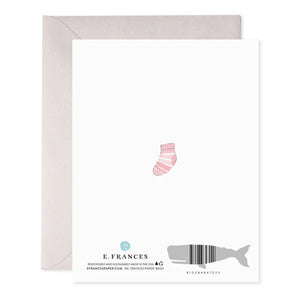 The E. FRANCES PAPER - BABY HEART GREETING CARD, by E. FRANCES PAPER, is handcrafted in the USA, featuring baby items like a rainbow, bib, bottle, bunny toy, onesie, stacking toys, pacifiers, and a wooden brush arranged in a heart shape with "hi baby!" at the center.
