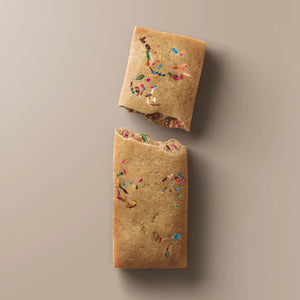 A wrapped STARS+HONEY - BIRTHDAY CAKE CHOCOLATE CHIP bar rests on a beige surface. The light blue packaging, branded with the STARS+HONEY logo and white text, displays nutrition details and hints at the irresistible flavors of vanilla yellowcake and natural sprinkles inside.
