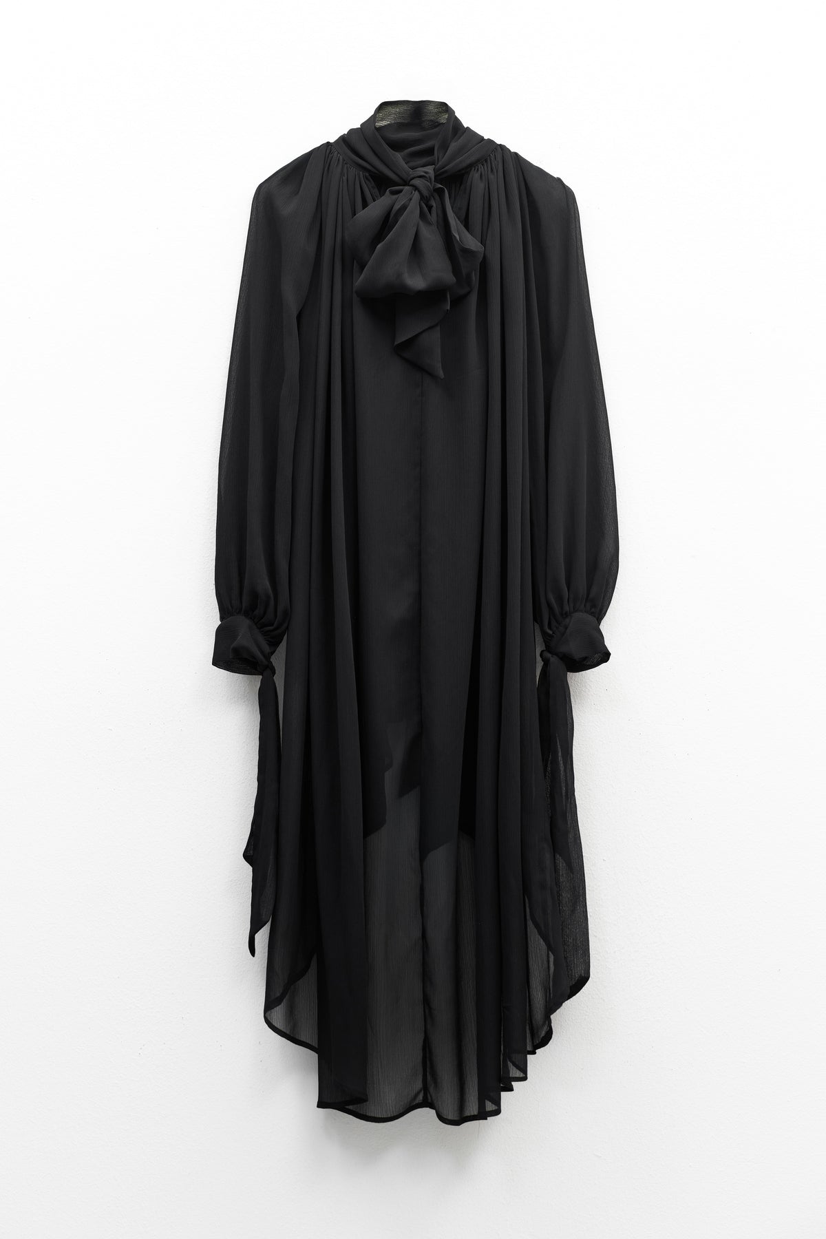 The ELEH - THE CHIFFON TIE NECK TOP by ELEH is a sheer black chiffon blouse with long sleeves, a high neckline, and an oversized bow tie at the collar—an elegant evening statement inspired by classic blouses.