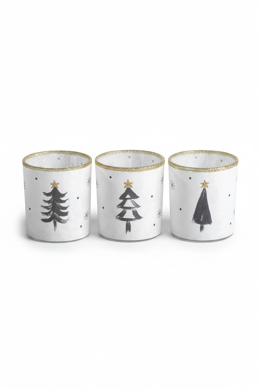 Three Zodax TREE TEALIGHT HOLDER cylindrical glass candle holders, sold individually, decorated with hand-painted black pine trees, gold glitter stars, and gold rims in an assorted style.