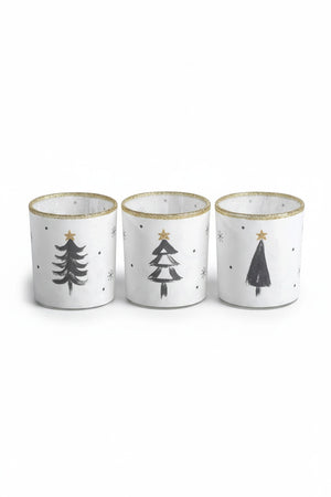 Three Zodax TREE TEALIGHT HOLDER cylindrical glass candle holders, sold individually, decorated with hand-painted black pine trees, gold glitter stars, and gold rims in an assorted style.