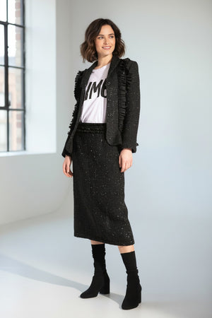 A woman wears the MEIMEIJ LUREX TWEED SKIRT with a black textured ruffle blazer, a white tee with black text, and black shoes with matching socks, posed against a white background.