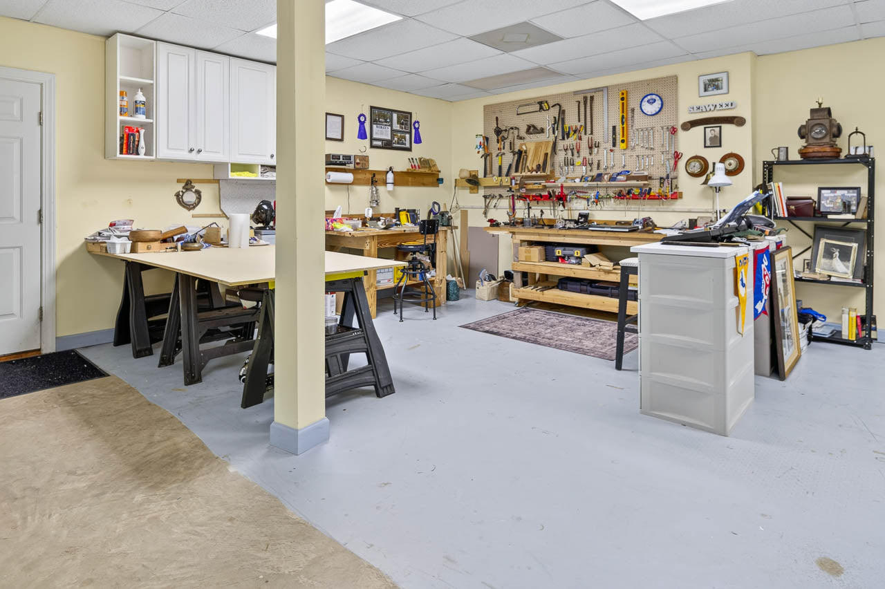 Spacious workshop with two workbenches, organized tools on pegboards, shelves with supplies, a filing cabinet, and wall decorations in a bright, clean room with white walls and ceiling.