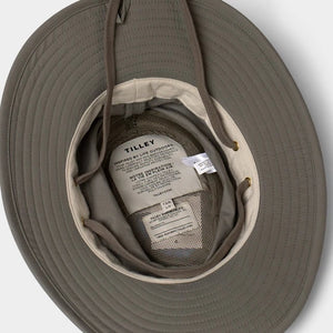 A man with a gray beard and mustache wears the TILLEY Airflo Hikers Hat T4MO-1 in olive, featuring UPF 50+ sun protection, and a beige button-up shirt, looking directly at the camera against a plain light background.