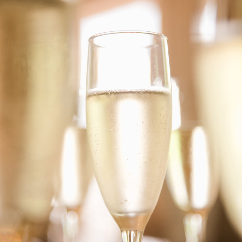 A close-up image of a champagne flute filled with FEARRINGTON VILLAGE&#39;s Champagne Wine Class showcases its effervescent splendor. The glass is delicately frosted with condensation, emphasizing its genuine quality. Blurred reflections of similar glasses can be seen in the background, enhancing a festive and sophisticated ambiance akin to exclusive wine classes.
