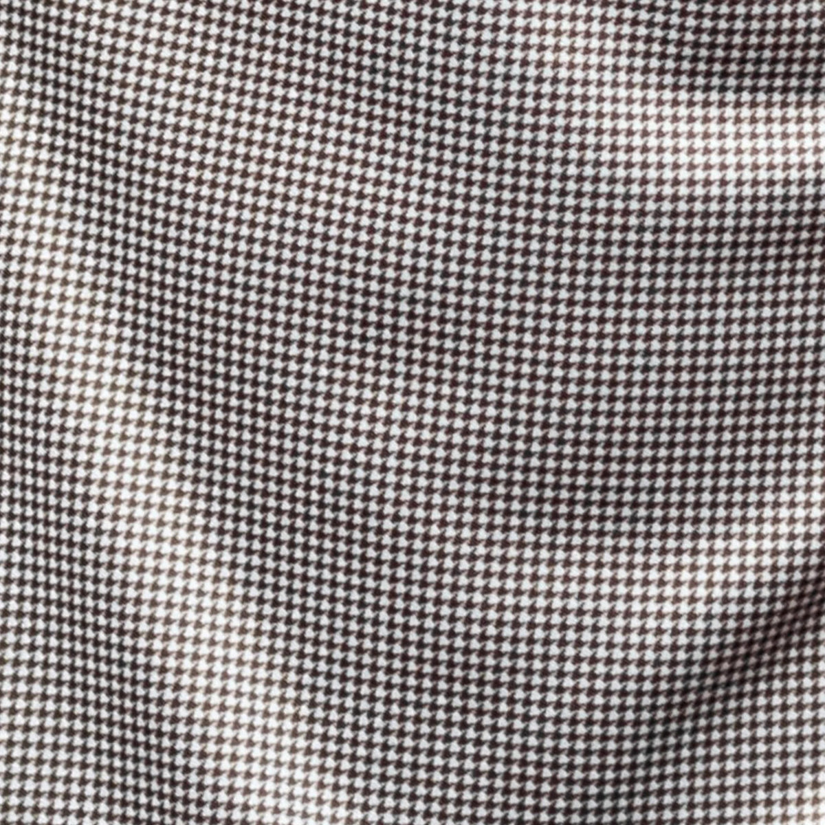 A man with short brown hair and a beard wears the COLLARS AND CO Semi Spread Collar Original Polo in Brown Houndstooth, standing in an urban setting with blurred buildings and warm outdoor lighting in the background.