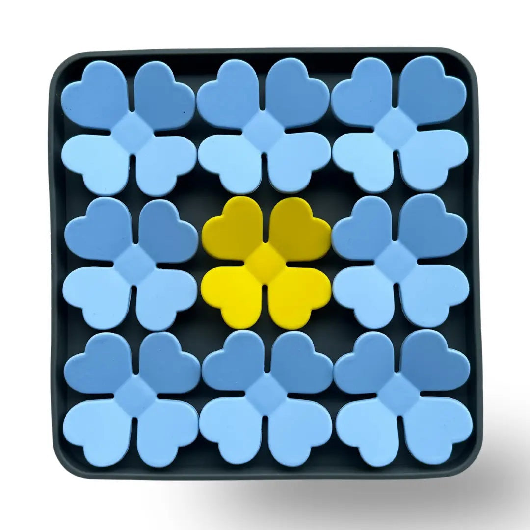 The BARKS & BROWNIES SNUFFLE MAT BOWL - BLUE features a tray with twelve four-petal flower shapes—ten in blue and two in yellow, with the yellow flowers placed at the center—all crafted from food-grade silicone for safe use as a dog slow feeder or snuffle mat bowl.