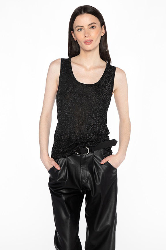 A woman with long, straight hair is wearing a KINROSS CASHMERE SHIMMER RIB TANK by KINROSS and black leather pants. She has her hands in her pockets and is standing against a plain white background. Her outfit subtly shimmers under the light, hinting at the inclusion of metallised fibers.