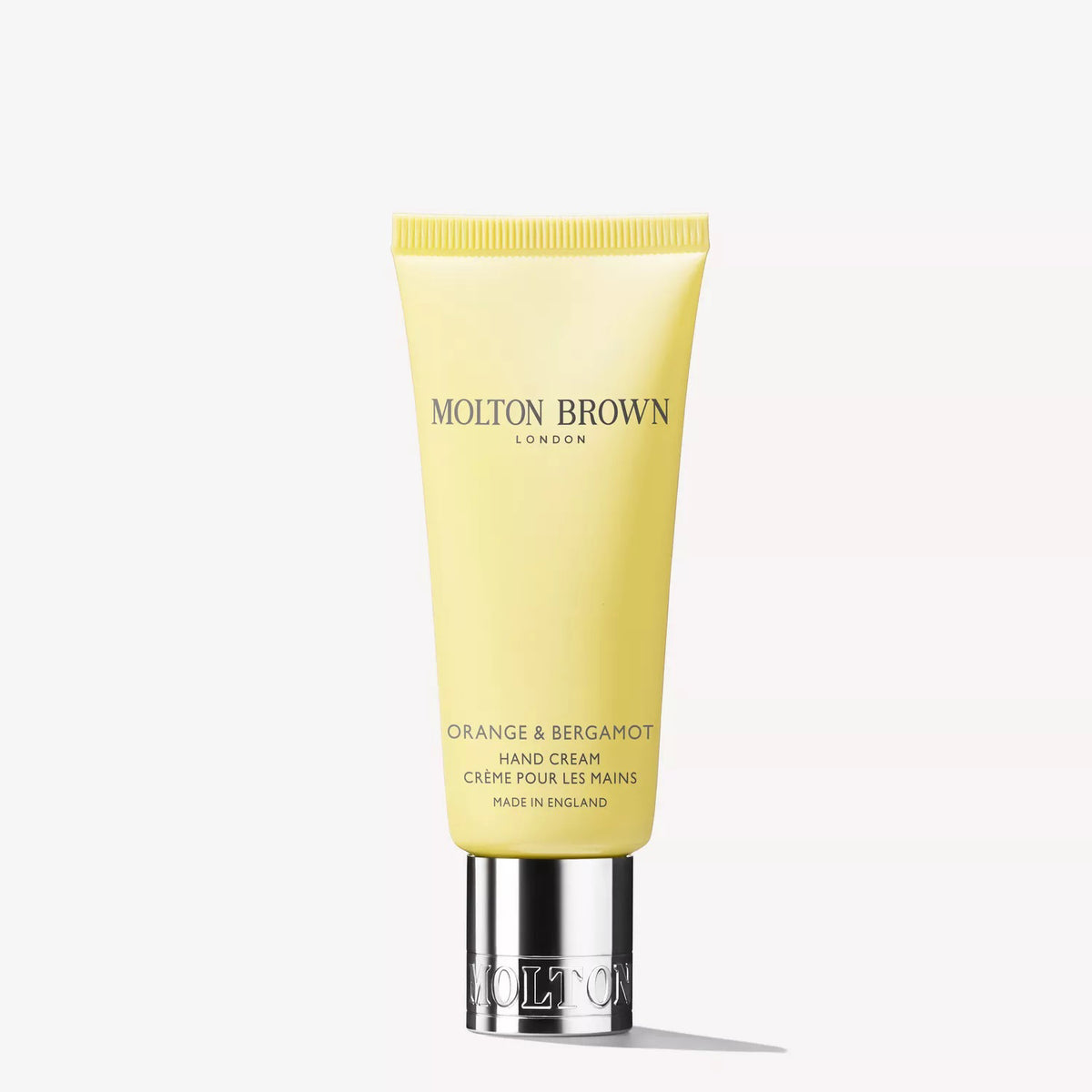 A yellow tube of MOLTON BROWN - ORANGE & BERGAMOT HAND CREAM with a silver cap, featuring fresh citrus musk notes, stands upright on a white background.