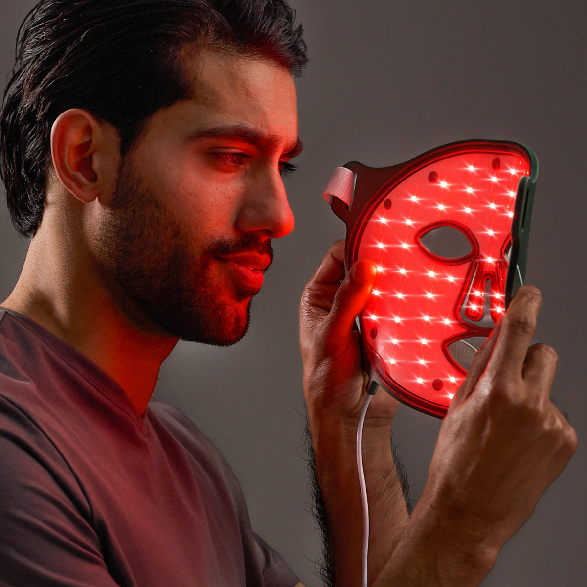 The OMNILUX - MENS MASK is a gray LED face mask with eye, nose, and mouth cutouts. &quot;Omnilux&quot; and &quot;Men&quot; are displayed on top. It uses red light therapy for men&#39;s skincare rejuvenation.