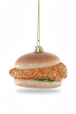 The SOUTHERN STYLE CHICKEN ORNAMENT by CODY FOSTER features a fried chicken sandwich design—bun, crispy patty, and pickle—hanging by a gold string. Perfect for collectors and design lovers to add a quirky touch to any tree.