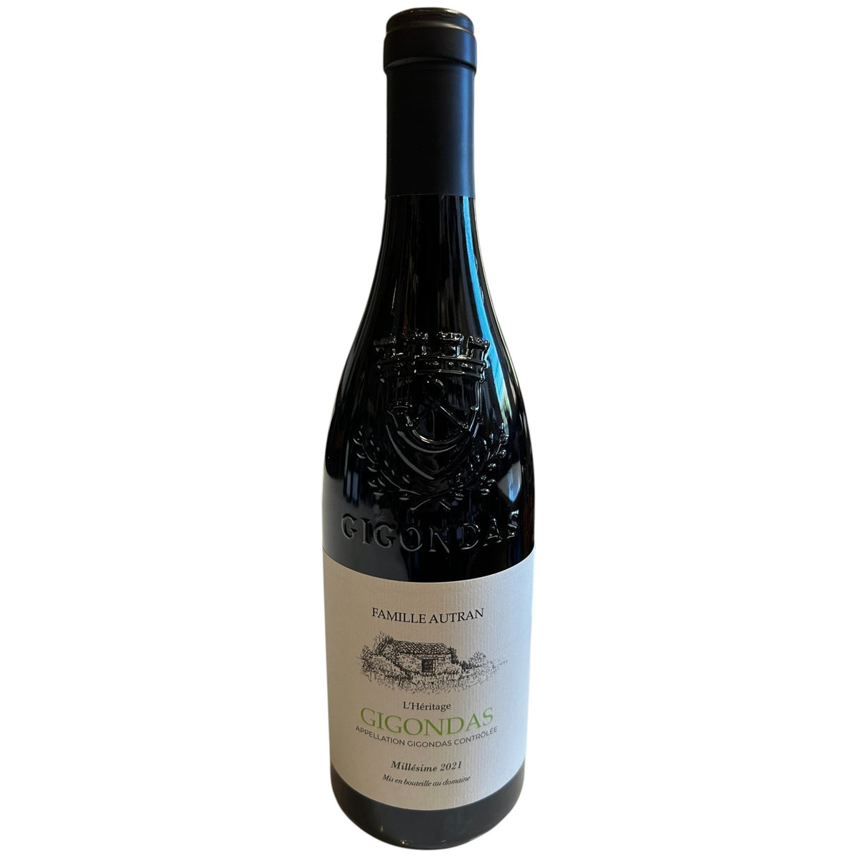 A bottle of FAMILLE AUTRAN GIGONDAS 2021 from WINE: PROOF rests on a white table in a restaurant, surrounded by wooden chairs, tables, and large windows in the background, embodying the elegance of Southern Rhône.