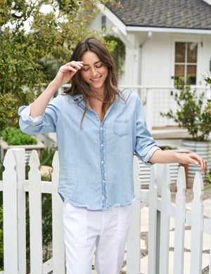 A light blue denim button-up shirt is displayed against a plain white background. The FRANK AND EILEEN - EILEEN RELAXED BUTTON UP CLASSIC WASH FAMOUS DENIM shirt features a relaxed fit, long sleeves rolled up to mid-forearm, a single chest pocket, and a slightly curved hem. Known for its bust-flattering button placement, the label inside reads "Frank & Eileen EST 1947.