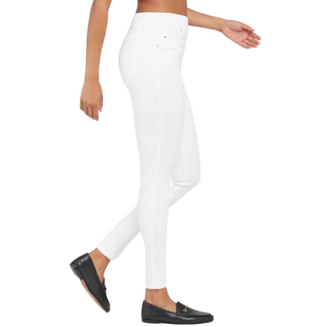 A person wearing the SPANX - SKINNY JEAN, which is a pair of high-waisted white skinny jeans crafted from stretch denim, and black loafers stands against a plain white background. The image focuses on the lower body, highlighting the jeans&#39; high-rise coverage and footwear.