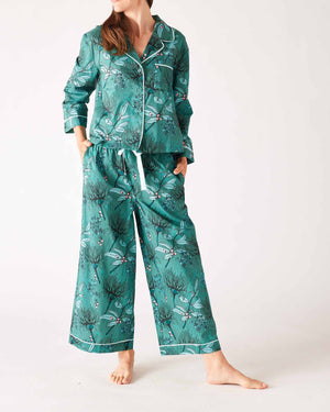A woman stands barefoot in the MERSEA - OVER THE MOON PAJAMA SET, a 100% cotton ensemble by MERSEA with vibrant red, teal, and white vertical stripes and arrow patterns; she has her hands in her pockets and long hair over one shoulder.