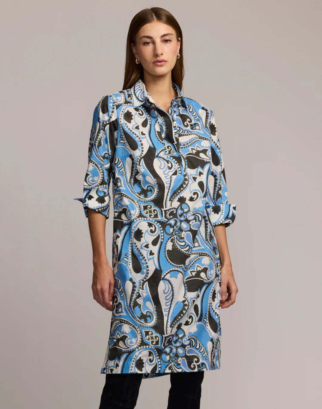 A woman wears the HINSON WU Charlotte 3/4 Sleeve Dress in Dancing Paisley, featuring a collared, button-up design in blue, black, and white. She stands against a plain background with her arms relaxed by her sides.
