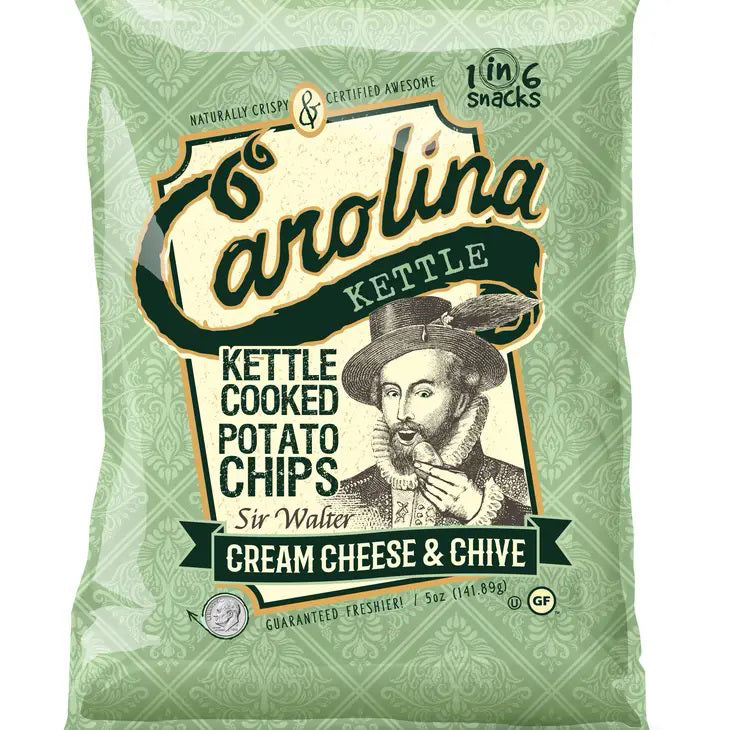 A bag of CAROLINA KETTLE - CREAM CHEESE AND CHIVE CHIPS by 1 IN 6 SNACKS features a vintage illustration of Sir Walter Raleigh. The enticing flavor combination is Cream Cheese &amp; Chive. The packaging design is green with white and dark green text, and includes "Gluten Free" and "1 in 6 Snacks" labels.