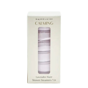 A BAUDELAIRE - CALM LAVENDER HAZE SHOWER STEAMER rests atop a slatted bamboo soap dish emblazoned with “BAUDELAIRE,” water droplets scattered on the white surface below—creating a tranquil scene evocative of soothing aromatherapy.