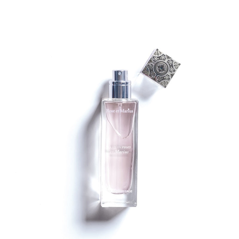 A rectangular ROSE ET MARIUS - LIFE IN ROSES Eau de Parfum 30ml bottle contains pale pink liquid. Inspired by Grasse perfumery, it features an intricate silver cap beside the bottle on a white background. Brand: ROSE ET MARIUS.