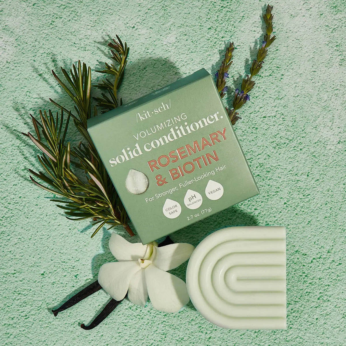 The image shows a box and curved light green bar of KITSCH's color-safe, pH-balanced, vegan Volumizing Solid Conditioner with rosemary and biotin, labeled "Kitsch Rosemary and Bioton Volumizing Solid Conditioner.