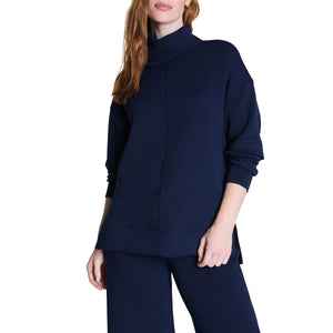 A woman in the SPANX AirEssentials Turtleneck Tunic in Timeless Navy displays a relaxed fit made with breathable spacer fabric for comfort.