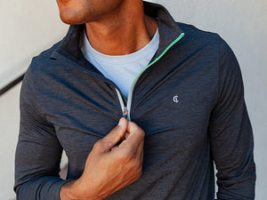 A man wears the CRIQUET Feather Performance Quarter Zip Pullover in Heather Black with a high collar and small chest logo, paired with blue jeans. His face is not visible; his arms are relaxed at his sides.