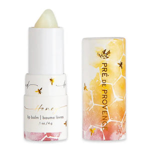 A tube of European Soaps, LLC Honey Lip Balm with its cap removed. The tube is mostly white with honeycomb and bee designs. The label text reads "lip balm, baume lèvres, .1 oz / 4 g." Infused with organic honey and royal jelly, the cap displays similar honeycomb and bee designs along with the brand's name.