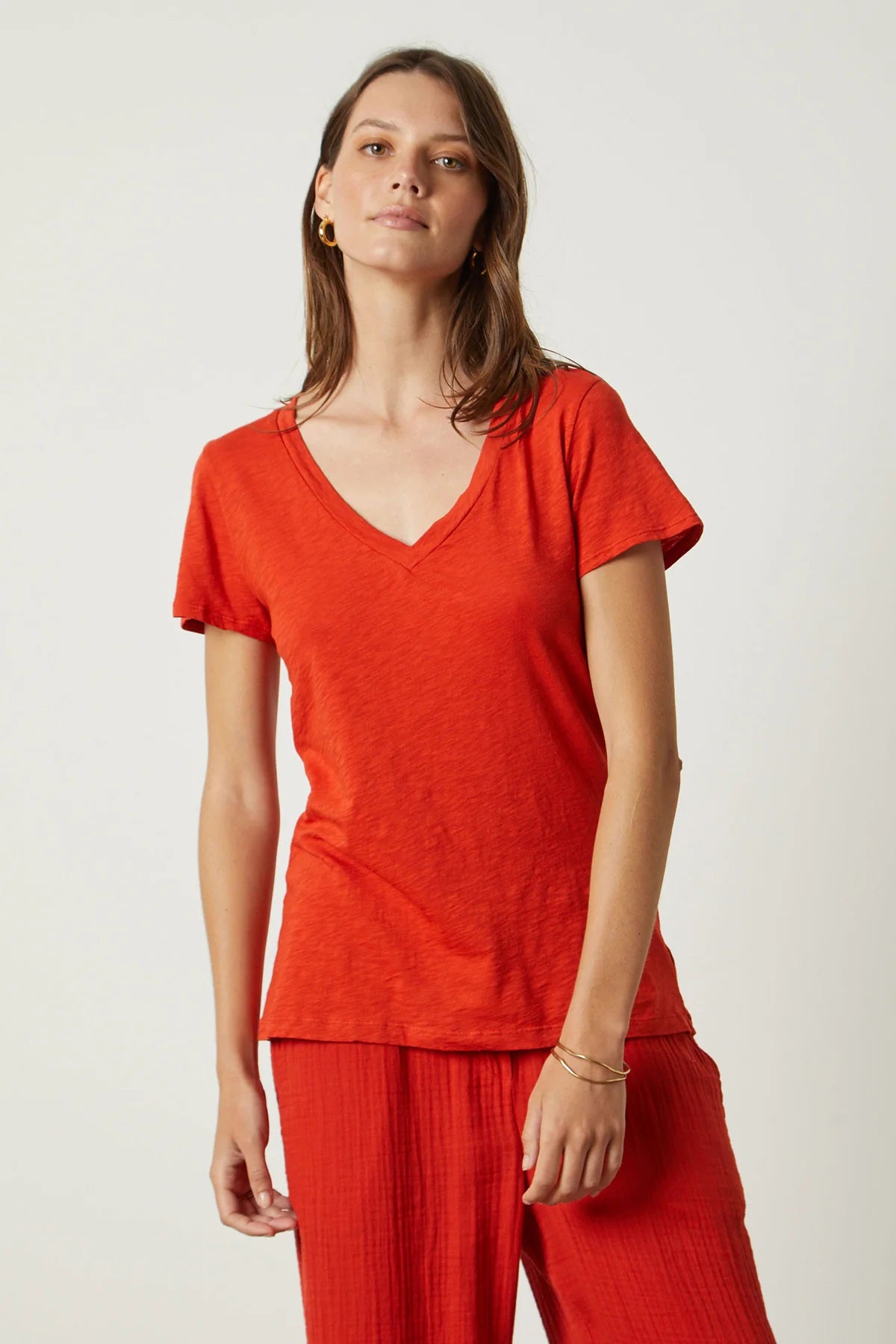 A person with shoulder-length brown hair is standing with their back to the camera. They are wearing a VELVET BY GRAHAM &amp; SPENCER&#39;s LILITH V NECK SLUB COTTON TEE in blue and light blue jeans. The background is a plain, light-colored wall.