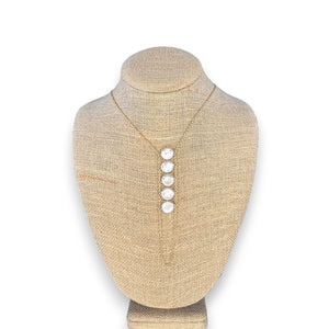 A woman in a beige top wears the GOLDISH - LADDERS TO BLISS PEARL NECKLACE, featuring round white stones, as she poses with crossed arms and a turned head, embodying balance and harmony.