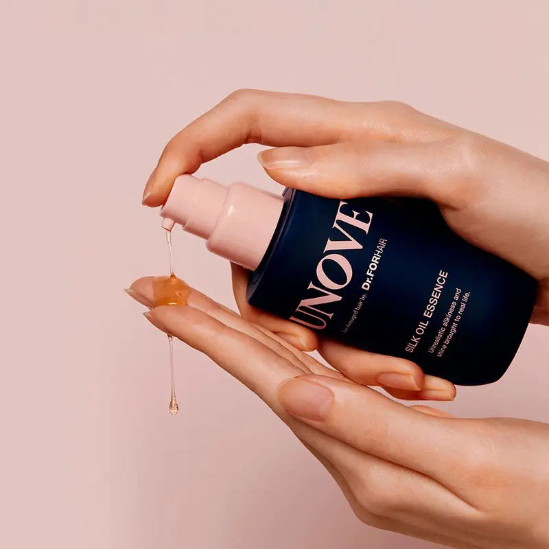 A blue UNOVE Silk Oil Hair Essence bottle from EXOD INTERNATIONAL, with a pink pump, offers lightweight nourishment for damaged hair. The label promises irresistible silkiness and shine for perfect frizz control, featured on a pristine white background.