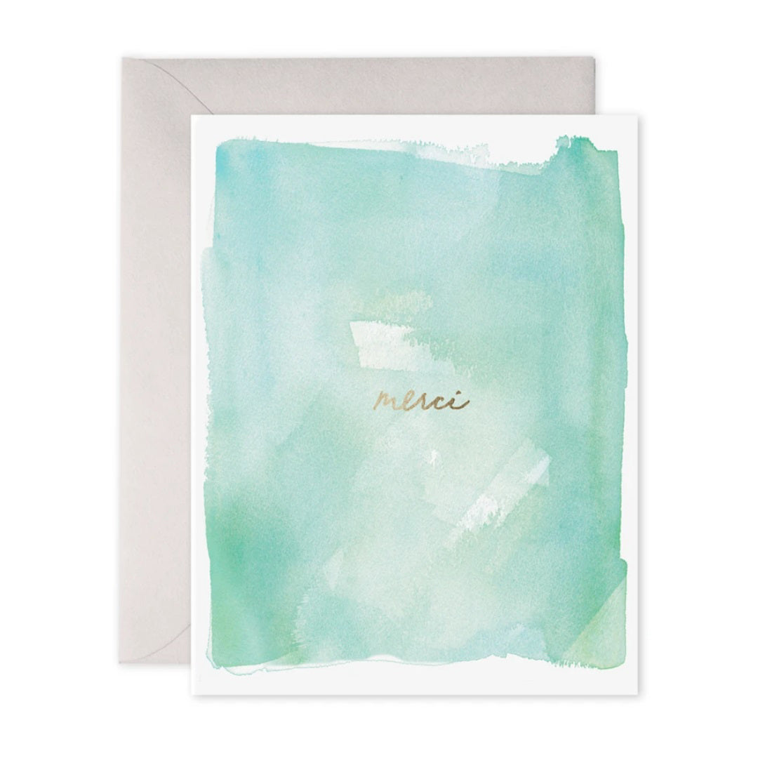The E. Frances Paper Merci Card showcases a pastel green and blue watercolor background, with "merci" scripted in gold cursive. It exudes positive energy and comes with a light gray envelope—perfectly blending Ali's artistry and sentiment.