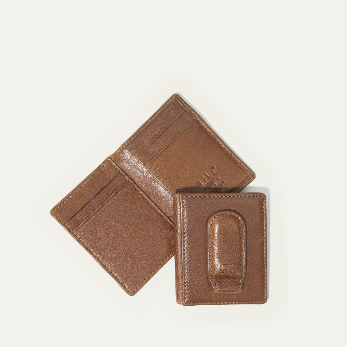 The WILL LEATHER GOODS Classic Money Clip sits atop an open full-grain leather wallet, both in brown, showcasing card slots against a plain light background.