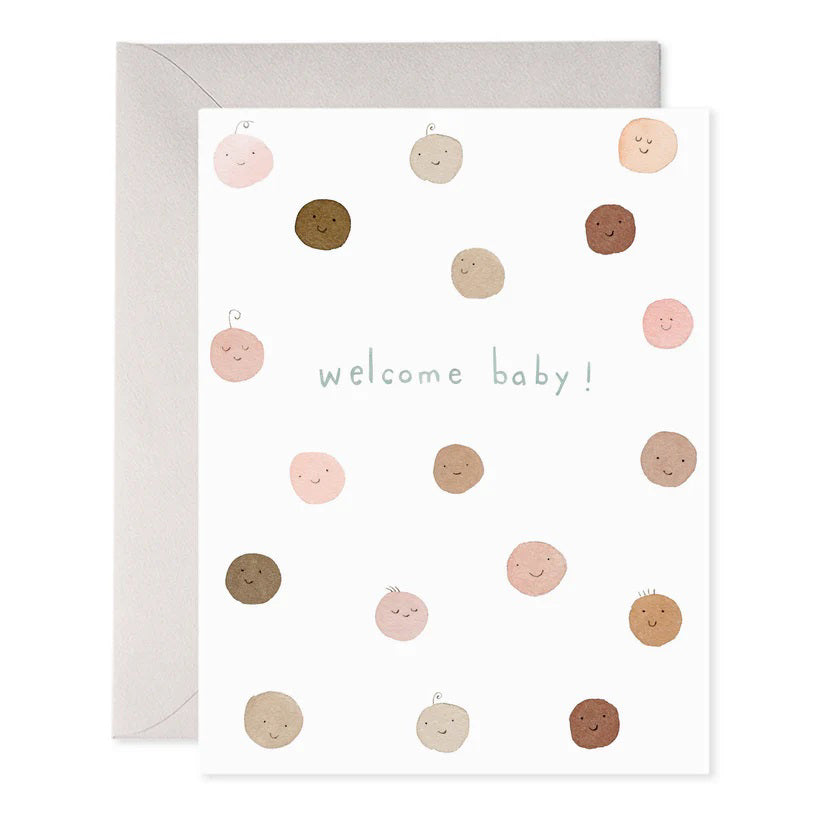 The E. FRANCES PAPER - WELCOME BABY GREETING CARD by E. FRANCES PAPER is a handcrafted watercolor card with "welcome baby!" in light blue, featuring smiling circular faces in diverse skin tones with little hair tufts, paired with a gray envelope, proudly made in the USA.