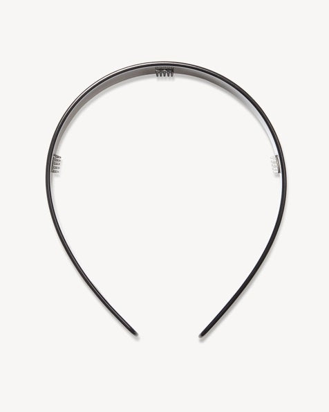 A woman in profile with a long braided ponytail wears a fuzzy beige sweater, gold hoop earring, and the MACHETE Wide Headband in Black by MACHETE. The background is plain off-white.