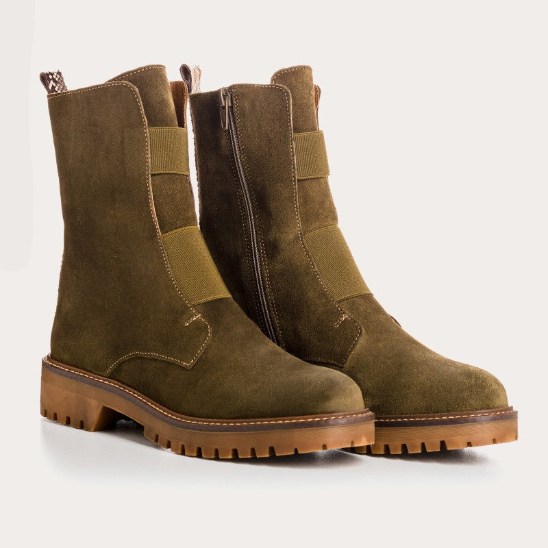 The REQINS Dusky Suede Ankle Boots in Khaki feature olive green suede leather, a chunky brown cleated heel, visible stitching, a pull tab at the back, and a rugged tread. A side zipper allows for easy wear.