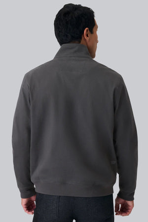 Close-up of a person wearing the MACK WELDON Twill Harrington Jacket in Shroom, featuring a zip front and buttoned flap pocket. Their arm is relaxed by their side and dark denim jeans are partially visible.