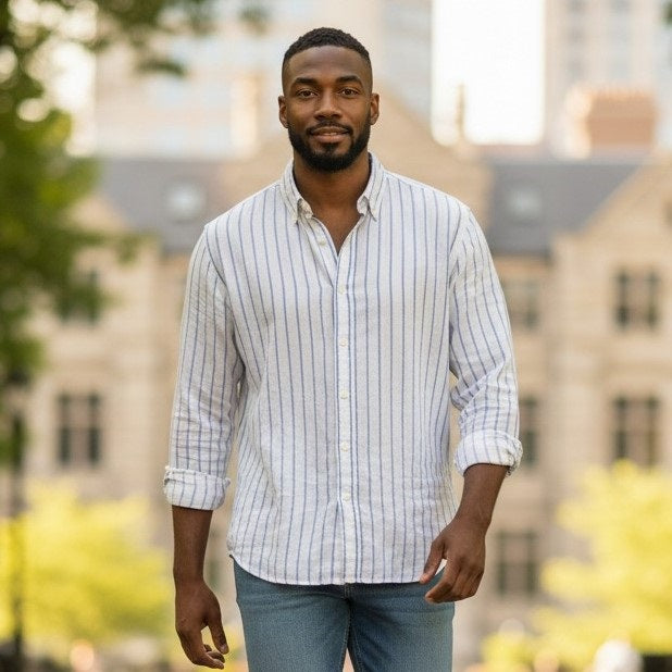 A man stands facing forward and smiling against a white background, wearing FRANK & EILEEN's FINBAR Men's Button Up Shirt in white with turquoise stripes (washed linen) and blue jeans.