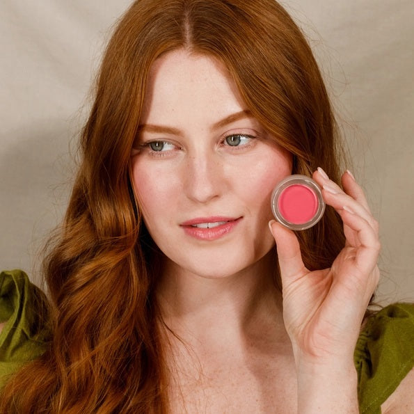 An open jar of MINORI - CREAM BLUSH in the shade Sweet Pea, featuring a pink lid and revealing a smooth, rosy pink cream-to-powder formula inside the clear container for a natural-looking blush finish.