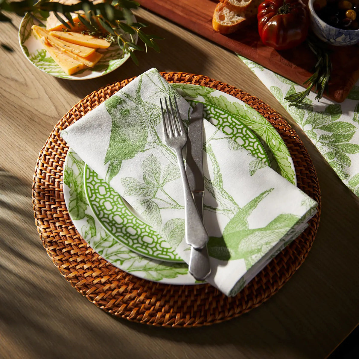 Four white cotton CASKATA - ARBOR BIRDS DINNER NAPKINS by CASKATA, made in India, are neatly stacked and display a repeating pattern of green birds on leafy branches.