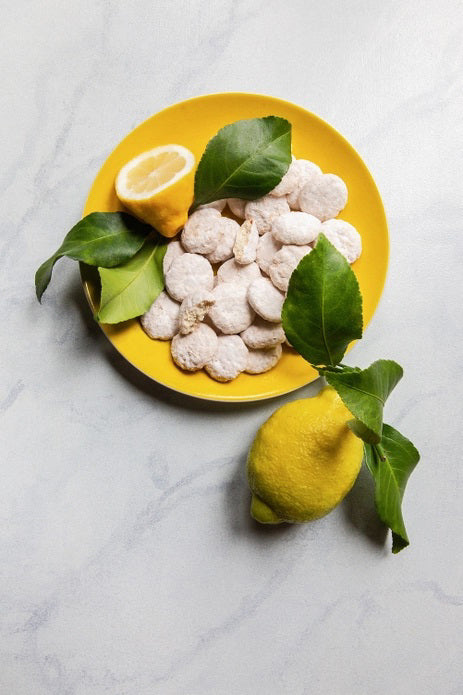 A yellow and green diamond-patterned box labeled "MEMAWS COUNTRY KITCHEN - LEMON COOLERS" from the brand 1 IN 6 SNACKS is pictured. The box displays images of sweet and zesty lemon cookies dusted with sugar. A blue silhouette of North Carolina with the word "made." is in the bottom right corner.