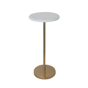 A green patterned armchair with a yellow throw is beside the CREATIVE COOP MARBLE TOP GOLD MARTINI TABLE. The table has a white marble top and seahorse-shaped gold pedestal base, supporting a vase and bowl; framed artwork decorates the white wall behind.