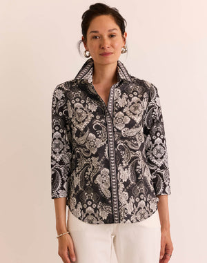 A woman models the HINSON WU - LIZETTE 3/4 SLEEVE PAISLEY PRINT SHIRT, a stylish black and white button-up crafted from premium cotton knit, featuring a paisley pattern and three-quarter sleeves. She pairs it with white pants and stands against a plain light background. This printed woven knits piece by HINSON WU is both fashionable and machine washable for easy care.