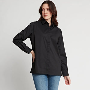 A person with medium-length dark hair wearing the HINSON WU SARA Long Sleeve Pleated Back Shirt, featuring a shirt collar and long sleeves, paired with black pants, stands against a plain white background. They have one hand in their pocket and are gazing slightly to the side, giving a relaxed and contemplative expression.