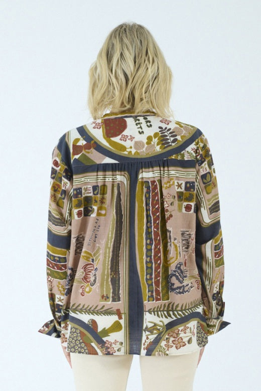 A person with blonde, shoulder-length hair is shown from the back against a plain light background, wearing the STORIATIPIC - MARGOT BLOUSE IN DELYS by STORIATIPIC—a colorful, patterned long-sleeve blouse crafted from 100% cotton for comfort and breathability. This top pairs effortlessly with light pants and is ideal for gentle machine wash and easy cotton care.