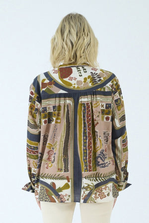 A person with blonde, shoulder-length hair is shown from the back against a plain light background, wearing the STORIATIPIC - MARGOT BLOUSE IN DELYS by STORIATIPIC—a colorful, patterned long-sleeve blouse crafted from 100% cotton for comfort and breathability. This top pairs effortlessly with light pants and is ideal for gentle machine wash and easy cotton care.
