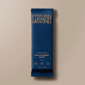 A blue wrapper labeled “STARS+HONEY - MAPLE BLUEBERRY MUFFIN”—a tasty collagen protein bar blending maple and blueberry flavors from the brand STARS+HONEY—rests on a beige surface, with nutritional information visible.